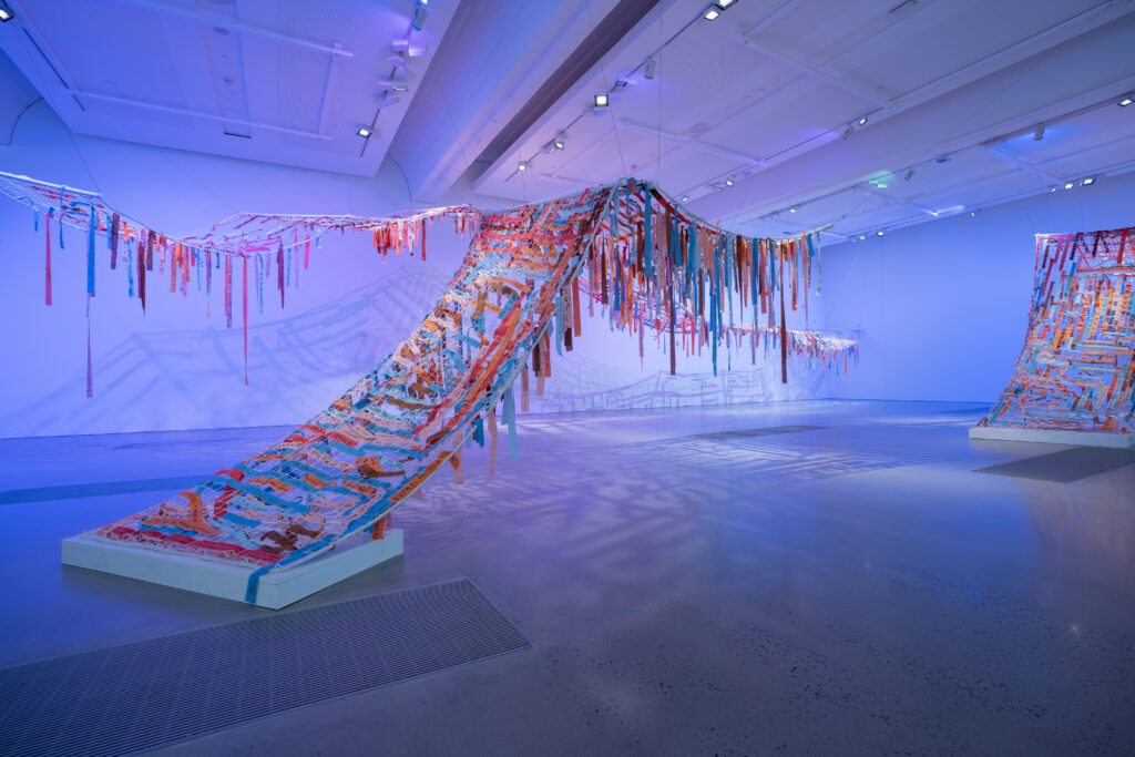 A textile artwork of nets and fabric strips hanging in a gallery space