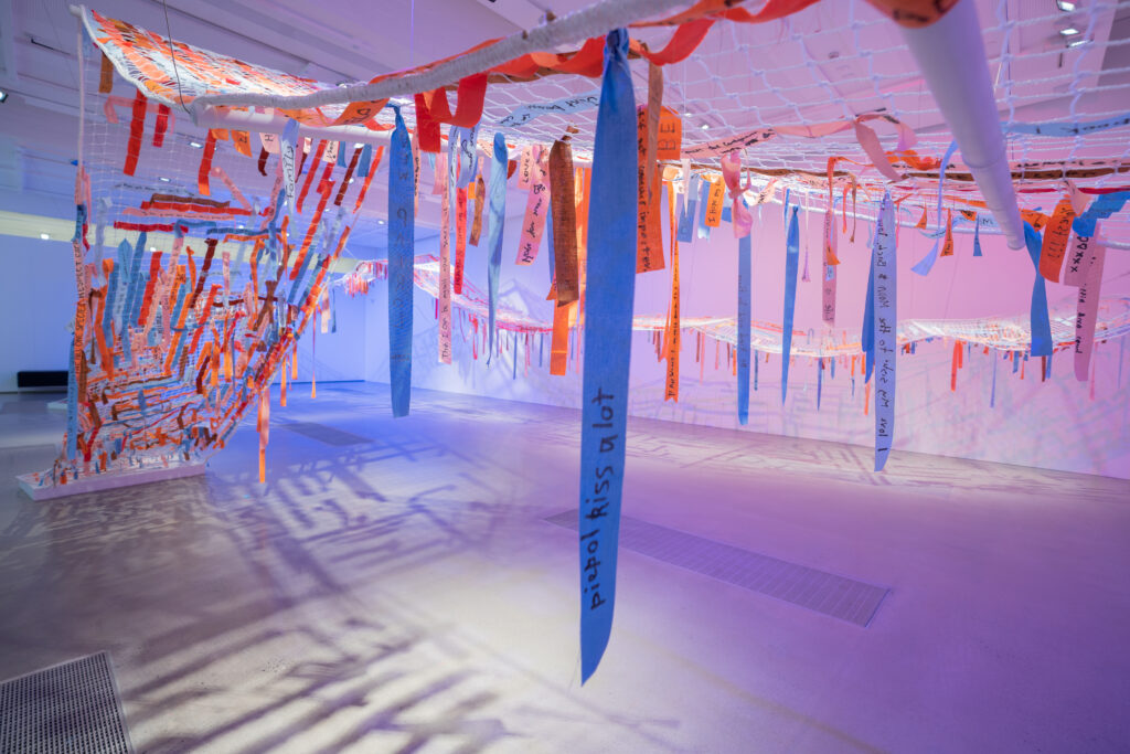 A textile artwork of nets and fabric strips hanging in a gallery space